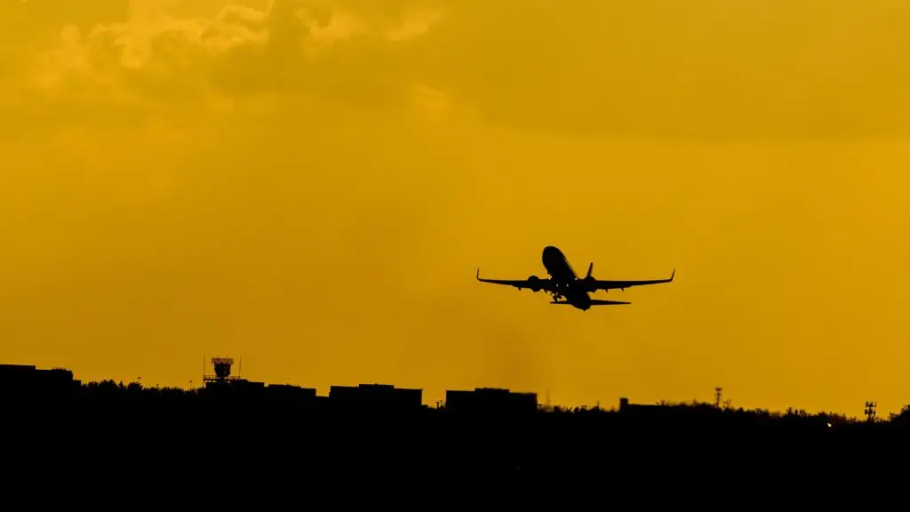 Samolot na tle pomarańczowego, wieczornego nieba. Pod samolotem widoczna jest linia horyzontu,