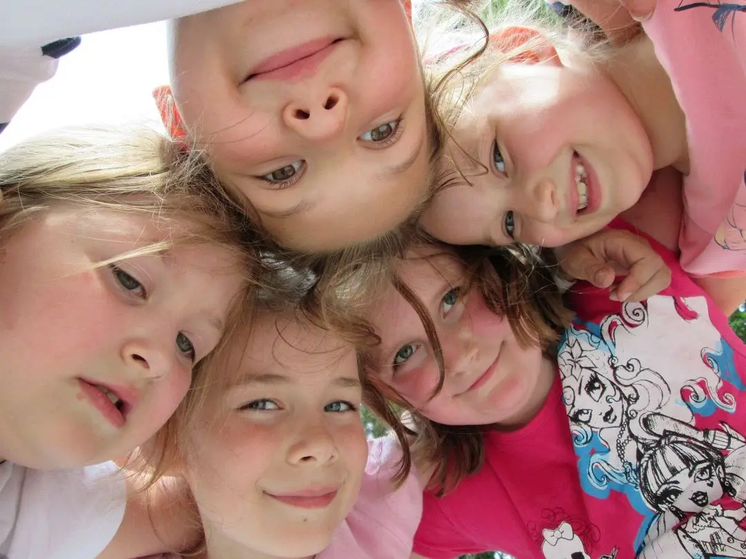 Pięcioro uśmiechniętych dzieci pochyla się nad obiektywem aparatu, stykając się głowami