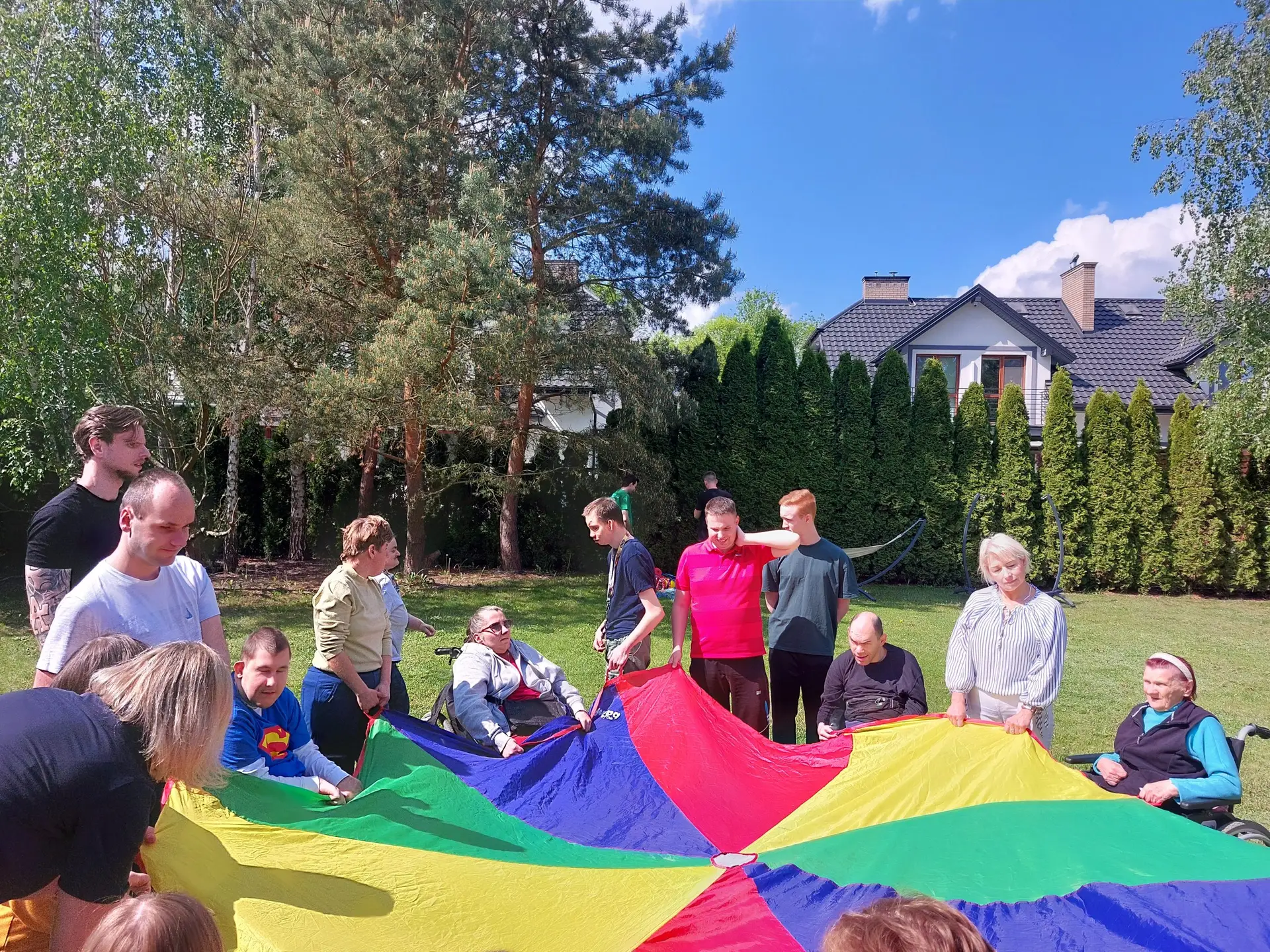 Podopieczni i opiekunowie Fundacji Nasza Bajka podczas zabawy z kolorową chustą w ogrodzie